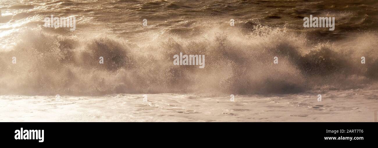 A line of white spray capturing the dramatic moment a wave breaks in a rough stormy sea sending white spray and waves high in to the air, motion and b Stock Photo