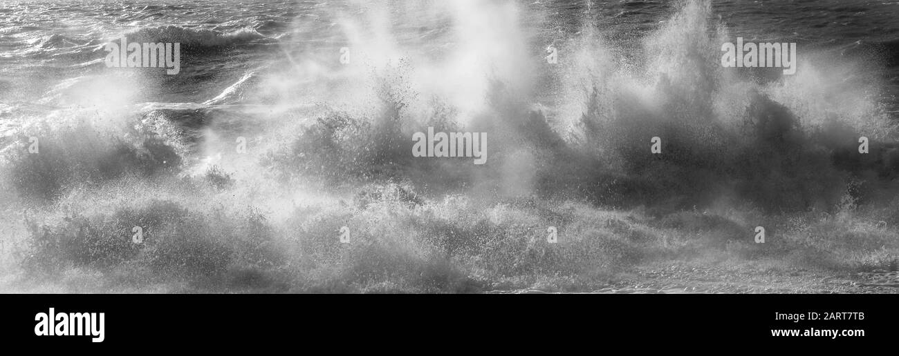 A line of white spray capturing the dramatic moment a wave breaks in a rough stormy sea sending white spray and waves high in to the air, motion and b Stock Photo