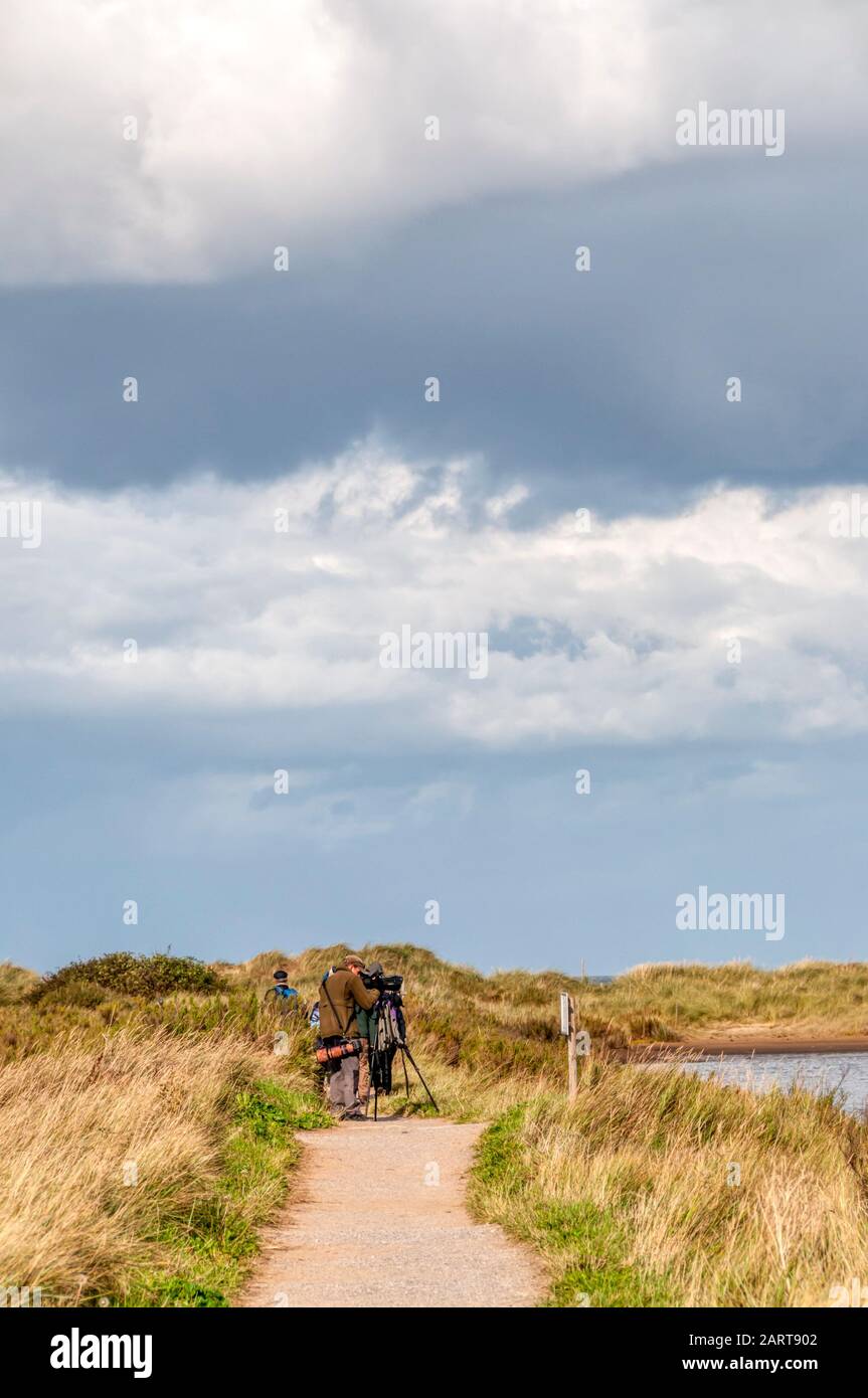 Bird watchers on the west bank path at the RSPB Titchwell Marsh bird reserve looking over the Tidal Marsh. Stock Photo