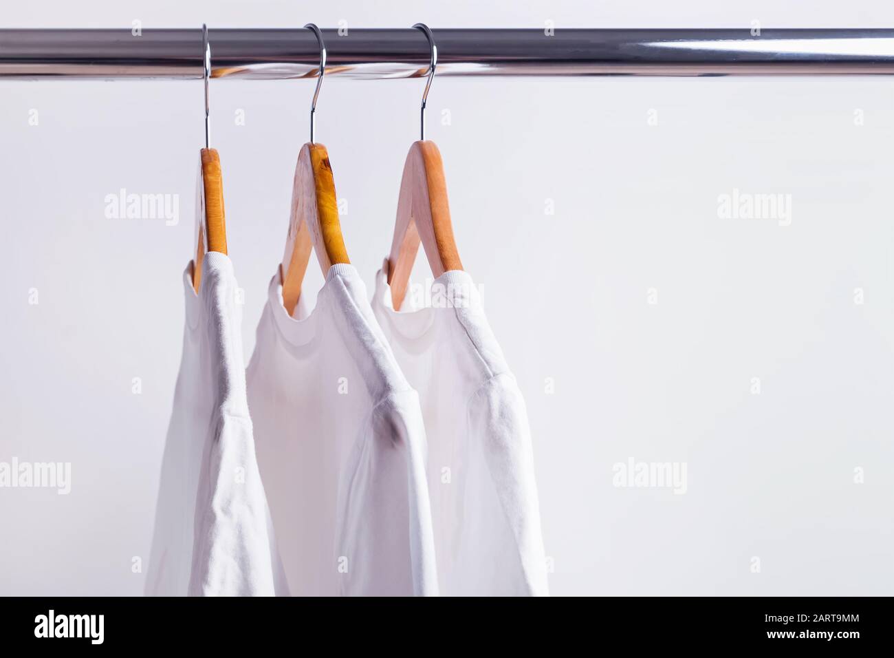 Three wite t-shirts hanging on wooden hangers Stock Photo