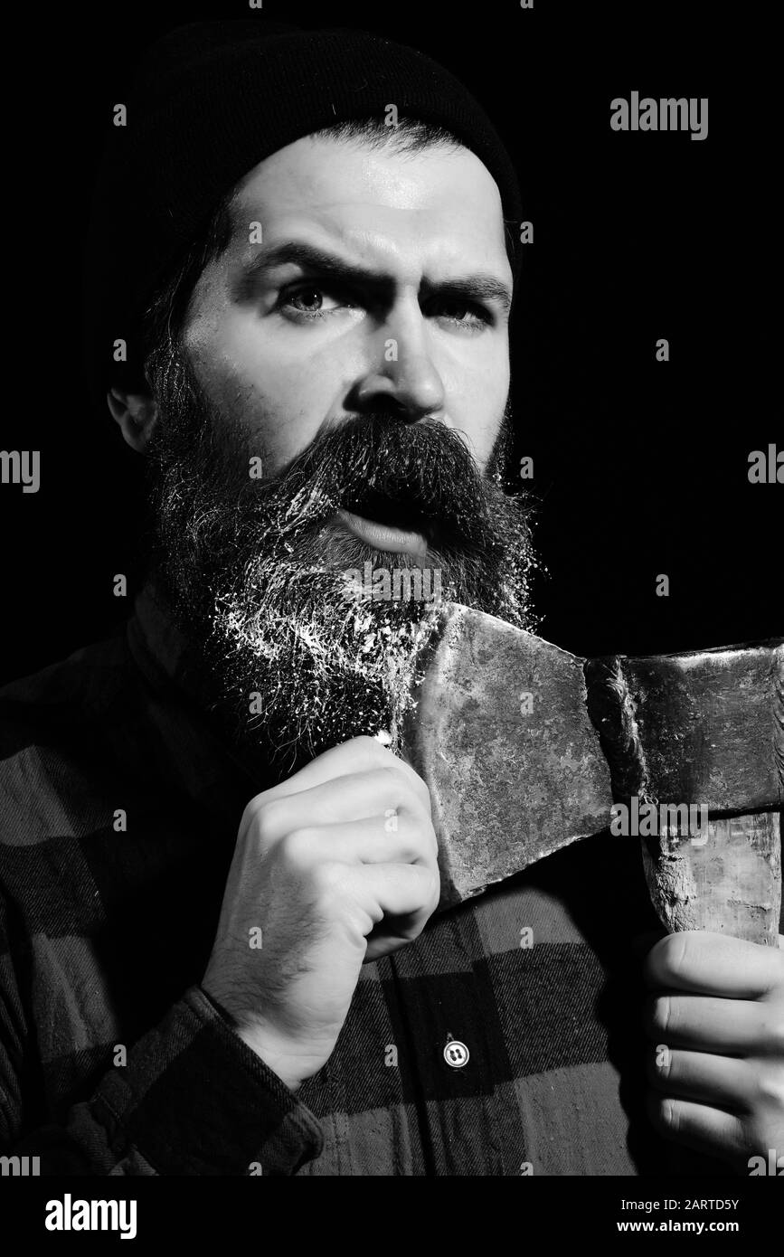 Scared man or lumberjack, bearded hipster with white beard and moustache, in hat keeps old rusty iron blade of axe on face isolated on black background Stock Photo