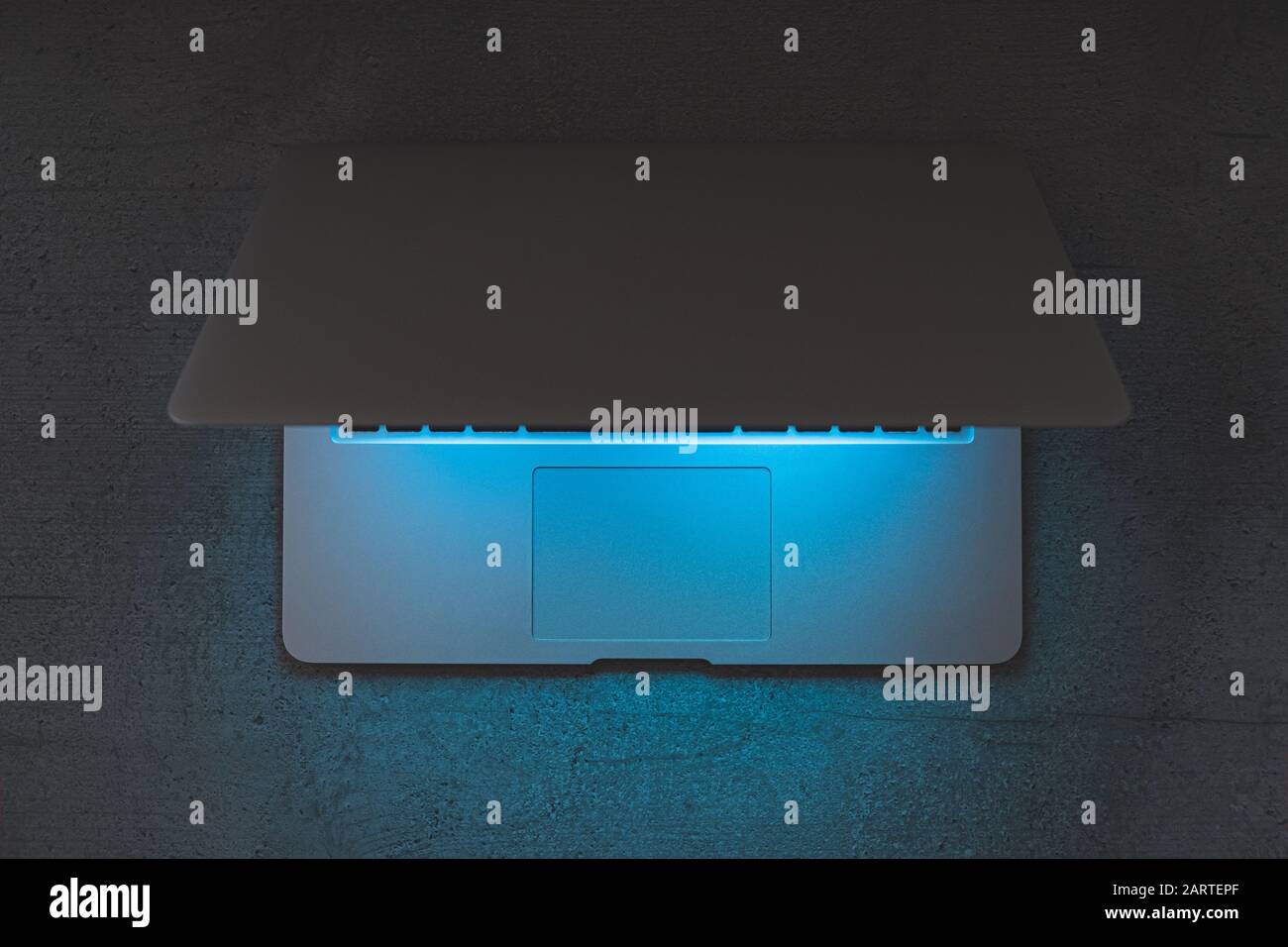 Top view of a laptop on a dark table, glowing blue screen. Minimalistic workplace, working with computer, using laptop at night and online privace con Stock Photo