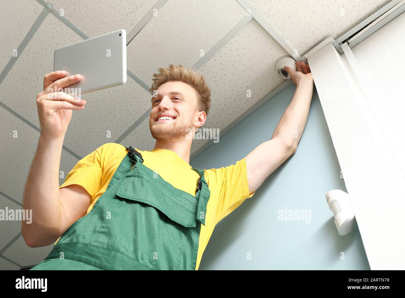 Electrician with tablet computer installing alarm system indoors Stock Photo