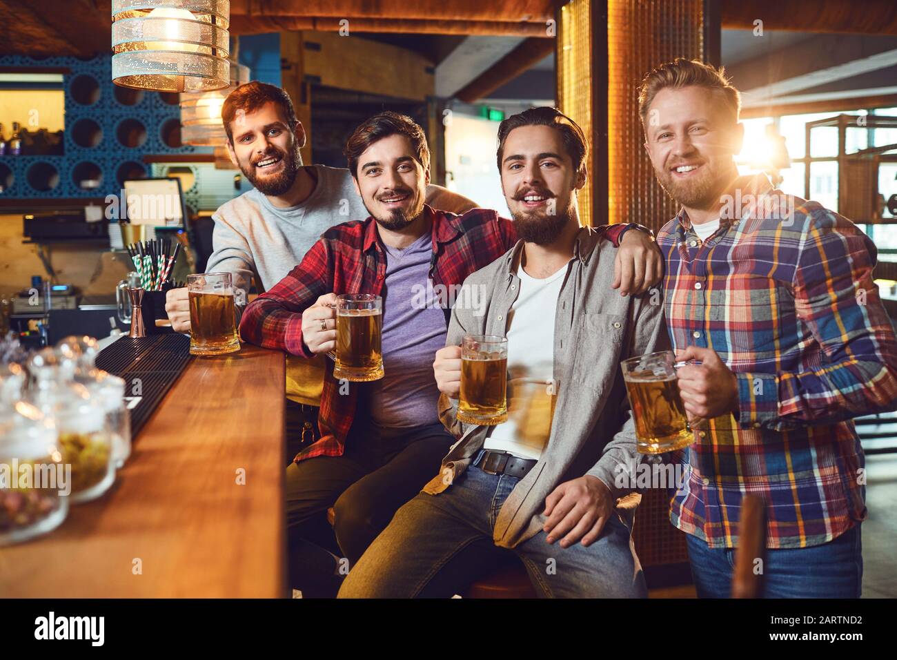 Friends with glasses of beer clinking while standing at a bar in a bar pub. Stock Photo