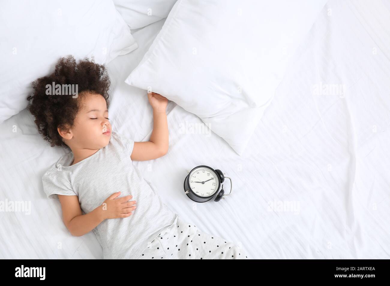 Little AfricanAmerican girl with alarm clock sleeping in bed Stock
