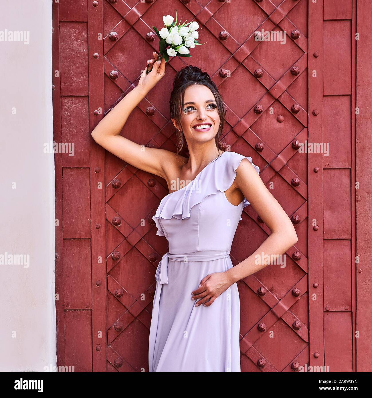 Beautiful bridesmaid girls brunette lady wearing elegant full length lavender violet tulle one shoulder maid dress and holding flower bouquet Stock Photo