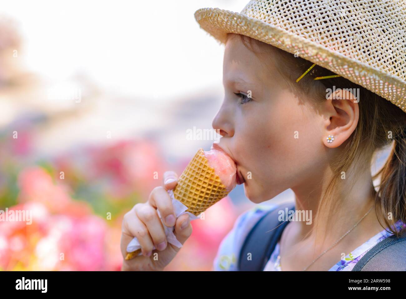Little girl in a straw hat eating ice cream in a cone on a summer sunny ...