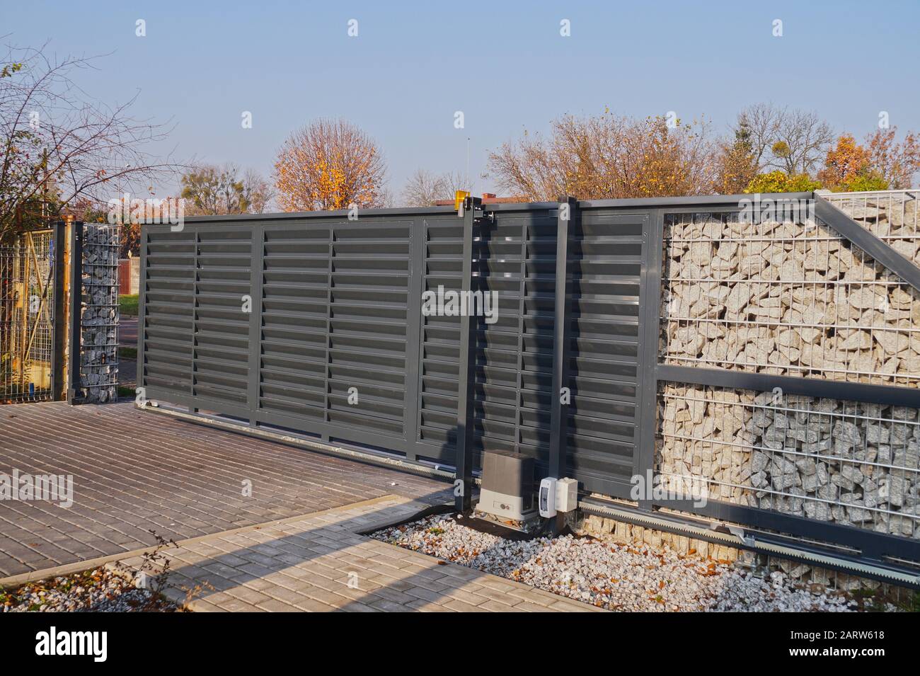 Automatic entrance gate used in combination with a wall made of gabion. Stock Photo