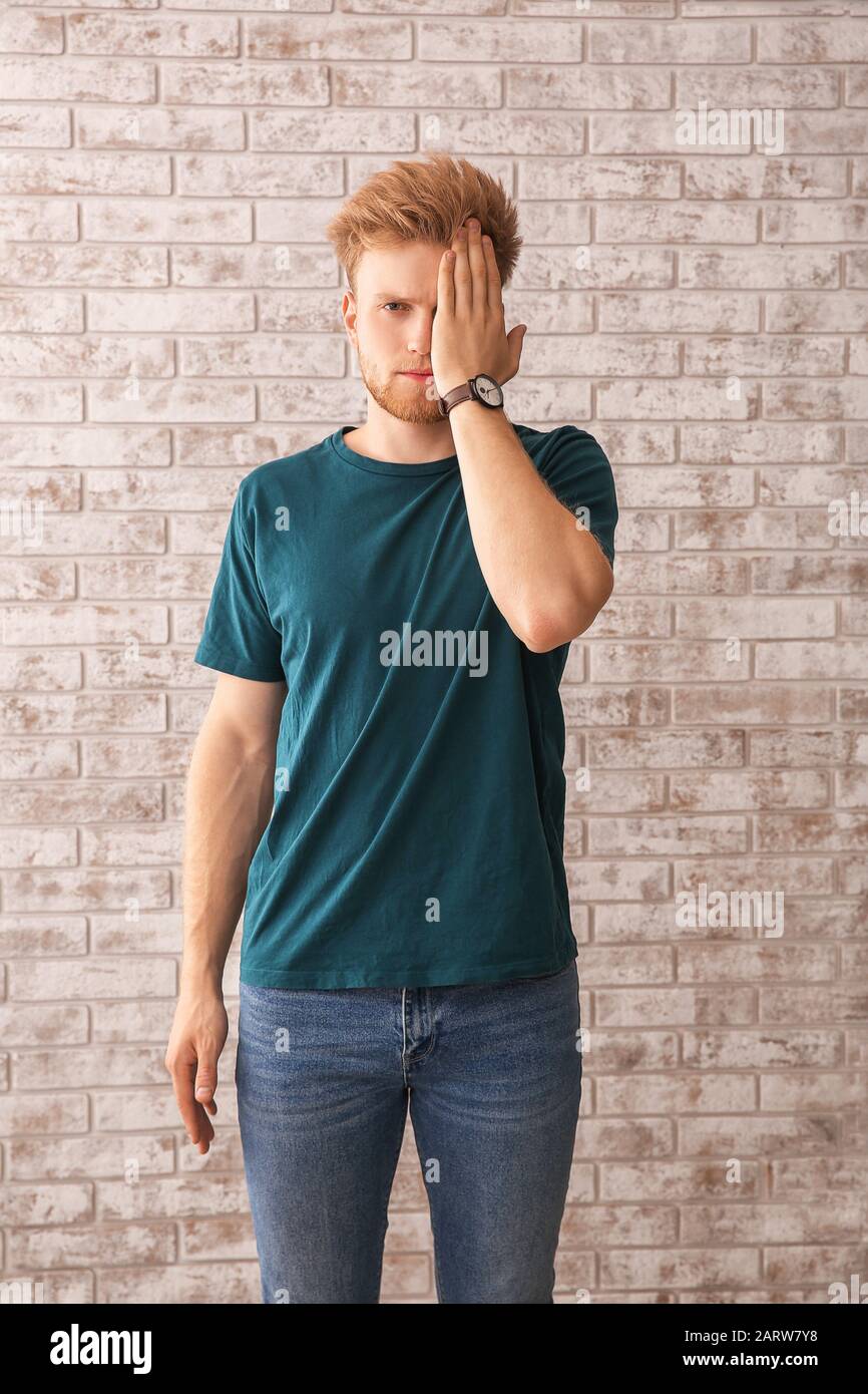 Portrait of young man covering eye with hand on brick background Stock ...