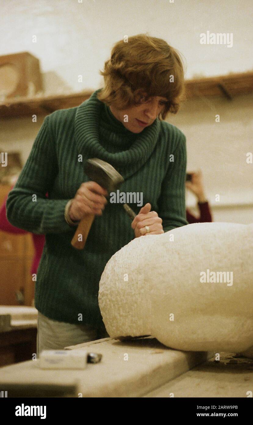 1970s, historical, female sculptor inside workshop at a bench working on a curved stone piece with hammer and small chisel, England, UK. Sculpture is a part of the visual arts, with durable sculptural a process where an artwork is made from carving and modelling a range of materials such as stone. Stock Photo