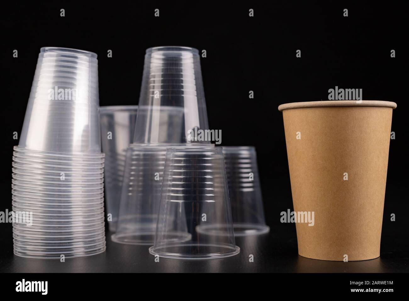 Plastic versus cardboard cups. Disposable tableware set on a table. Dark background. Stock Photo