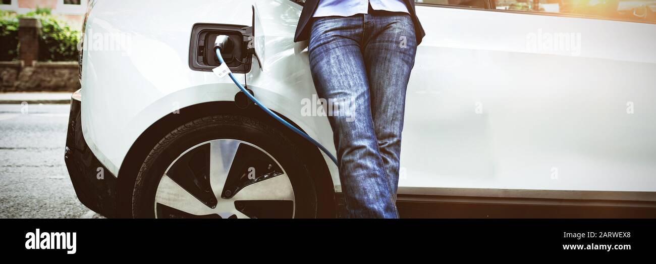 Businessman using digital tablet while charging electric car at charging station Stock Photo