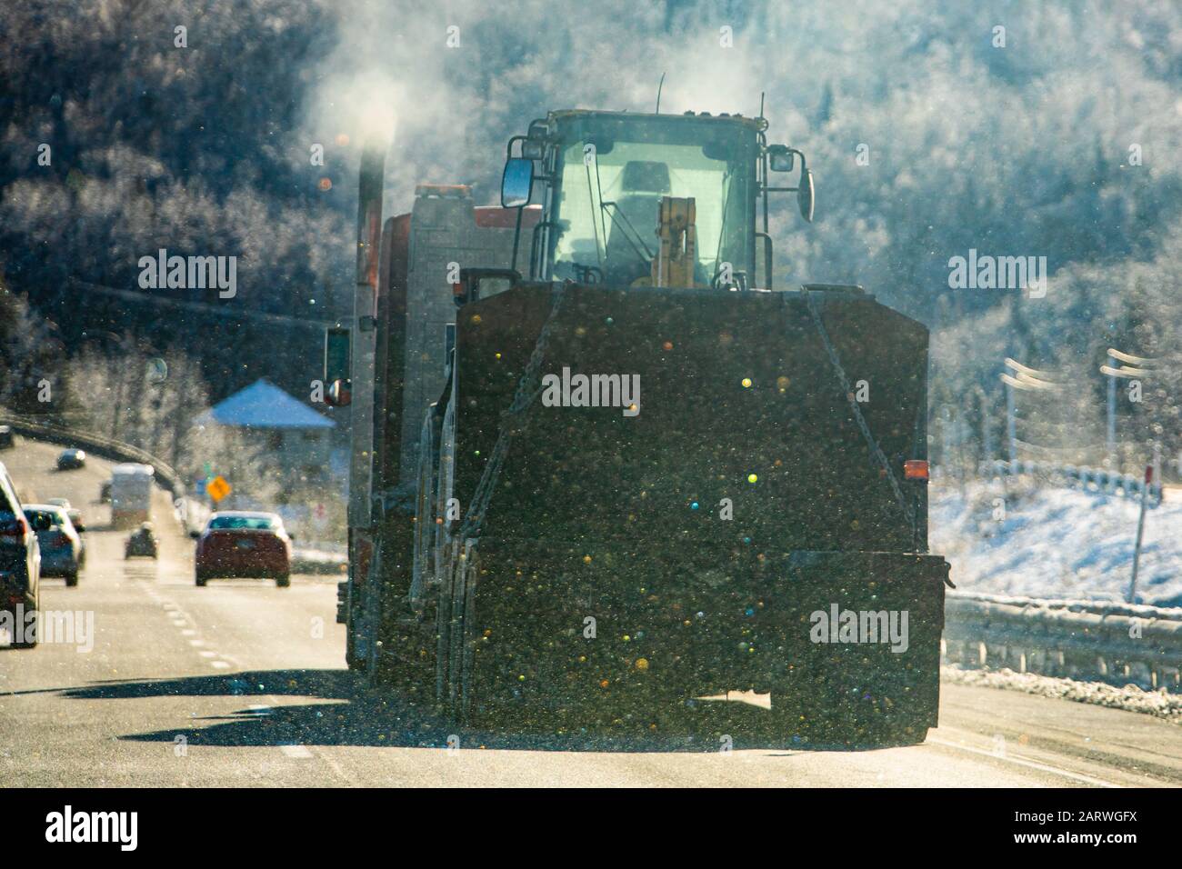 A soft focus shot, with light snowfall and colorful refractions, of a heavy articulated truck hauling an agricultural tractor on a highway in winter Stock Photo