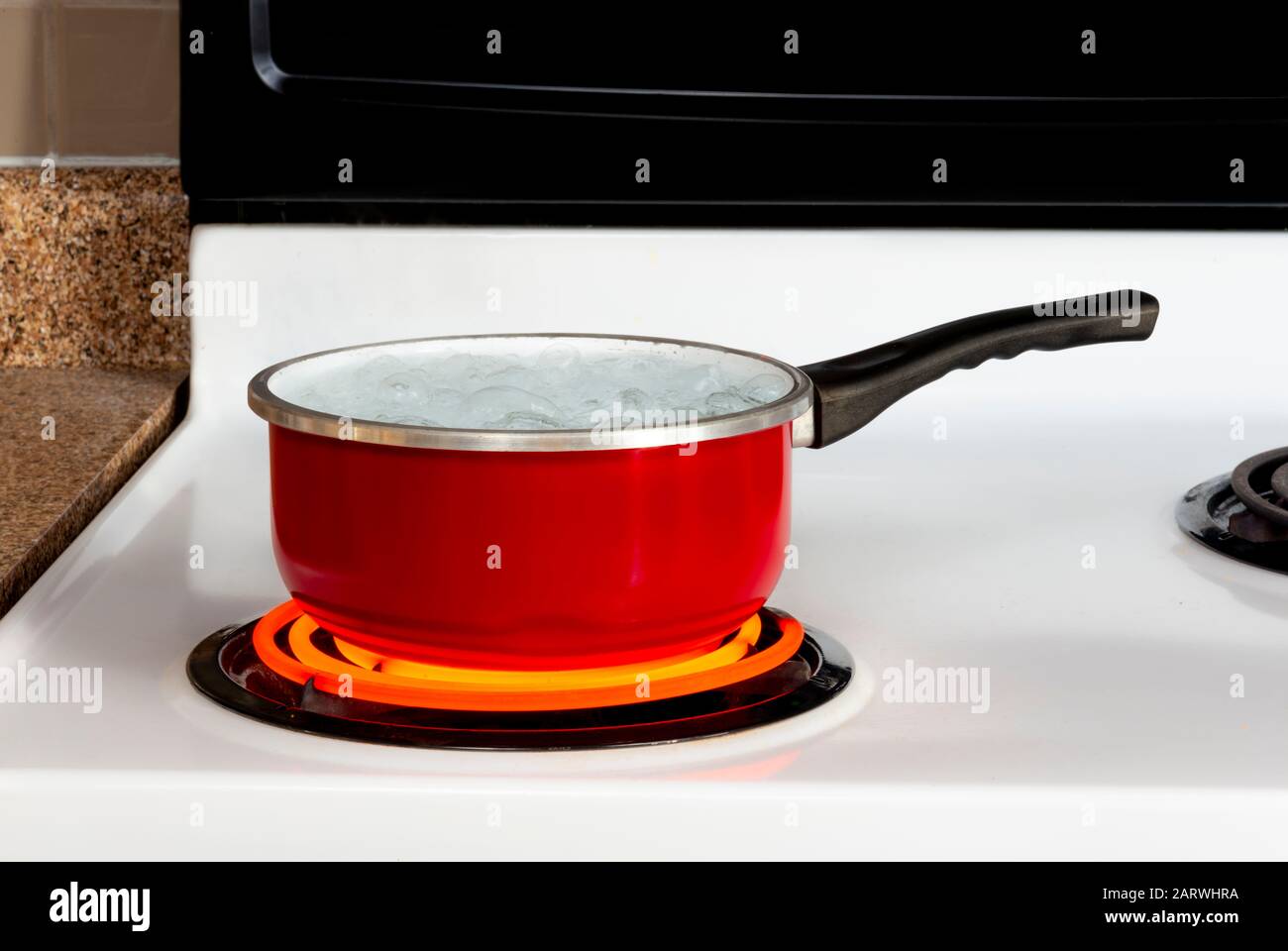 Horizontal shot of a red pan of boiling water on top of a stove with the burner turned to high. Stock Photo