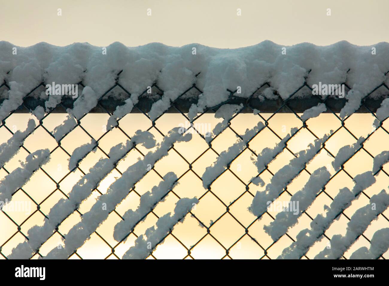 A close up soft focus shot of a chain link fence, aka diamond mesh, hurricane fencing, wire netting boundary, covered with snow during golden hour Stock Photo
