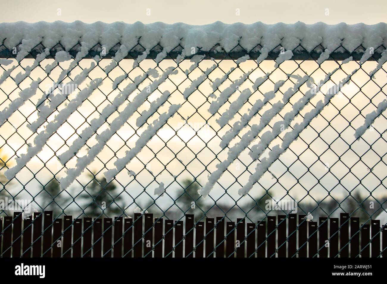 A selective focus view of a chain link diamond mesh fence creating a barrier during winter, covered in white snow and ice against a muted sky Stock Photo