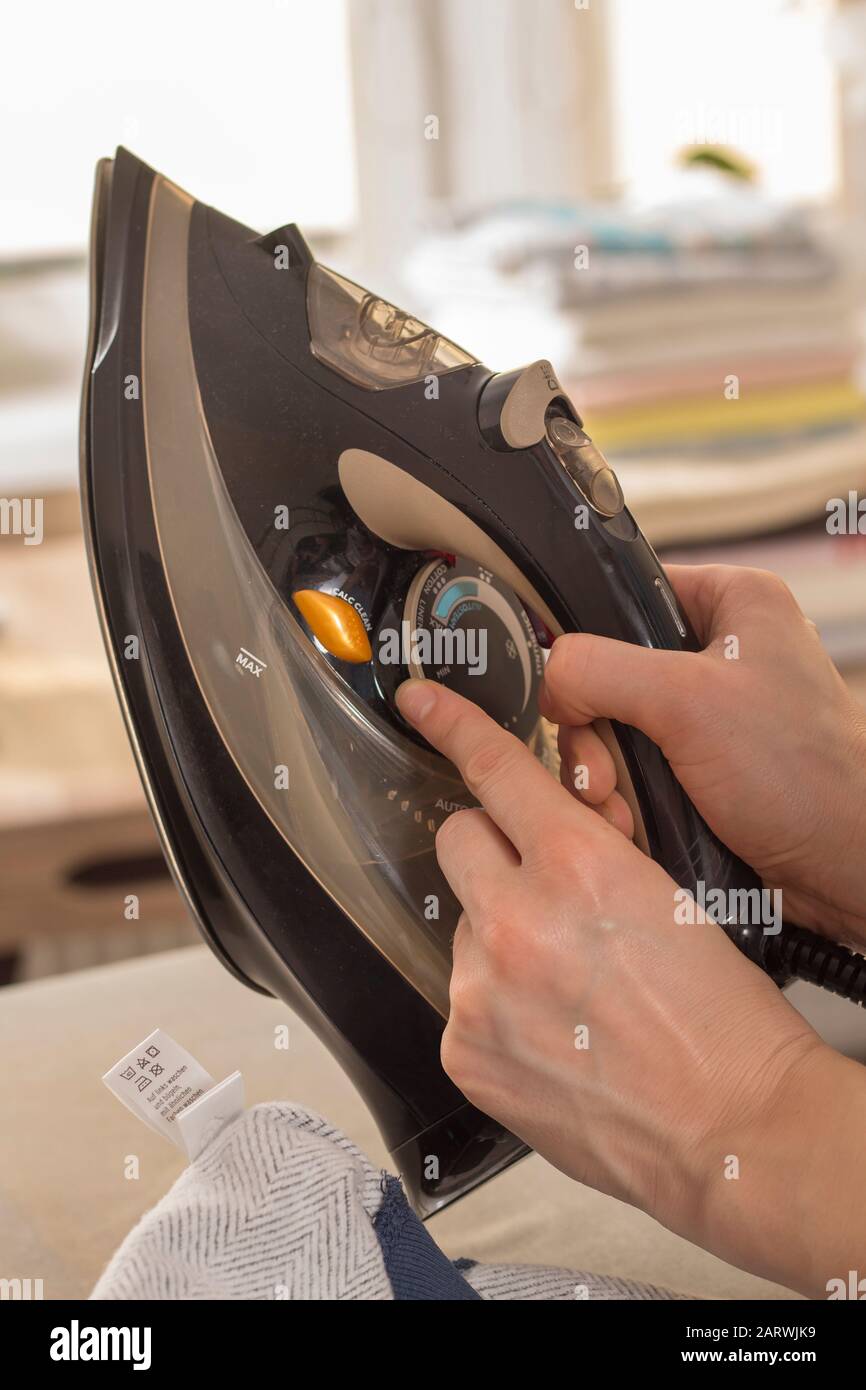 A woman's hand holds the iron and sets the right ironing temperature