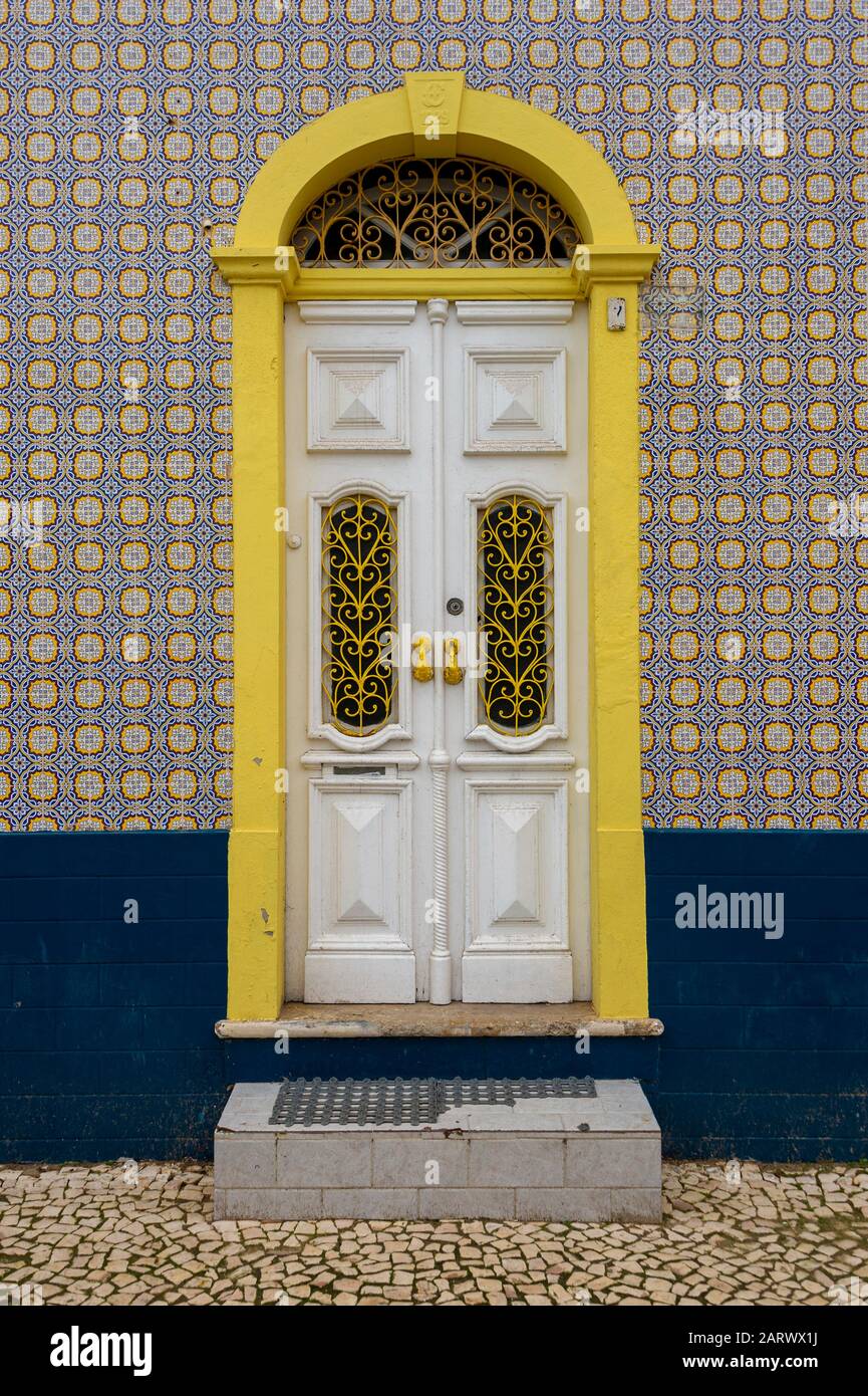 Portugal, facade of a house covered with typical ceramic azulejos tiles and a decorated wooden door in white and yellow Stock Photo