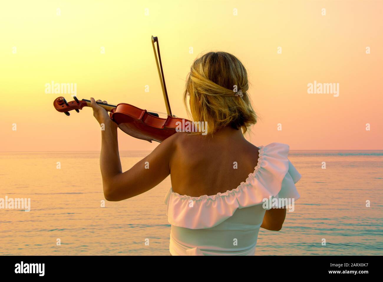 Beautiful woman playing violin at the sea with sunset background Stock Photo