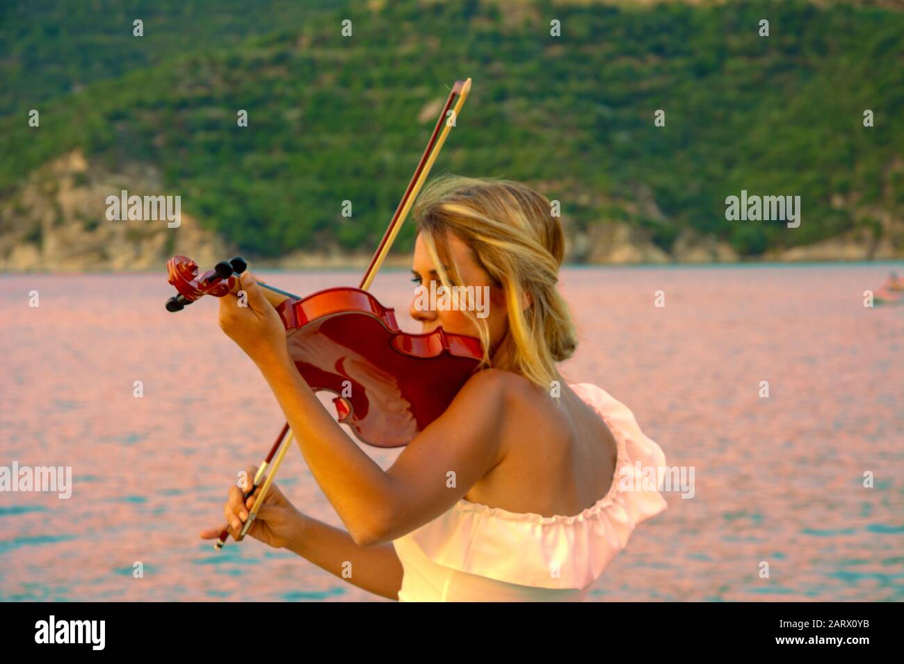 Beautiful woman playing violin at the sea with sunset background Stock Photo