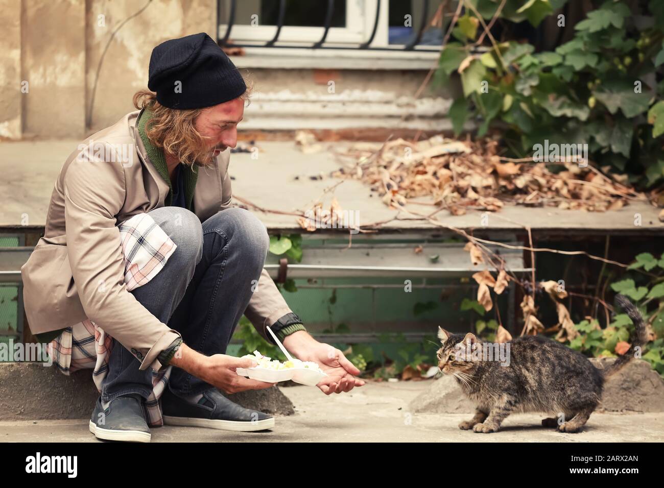 Poor man sharing food with homeless cat outdoors Stock Photo