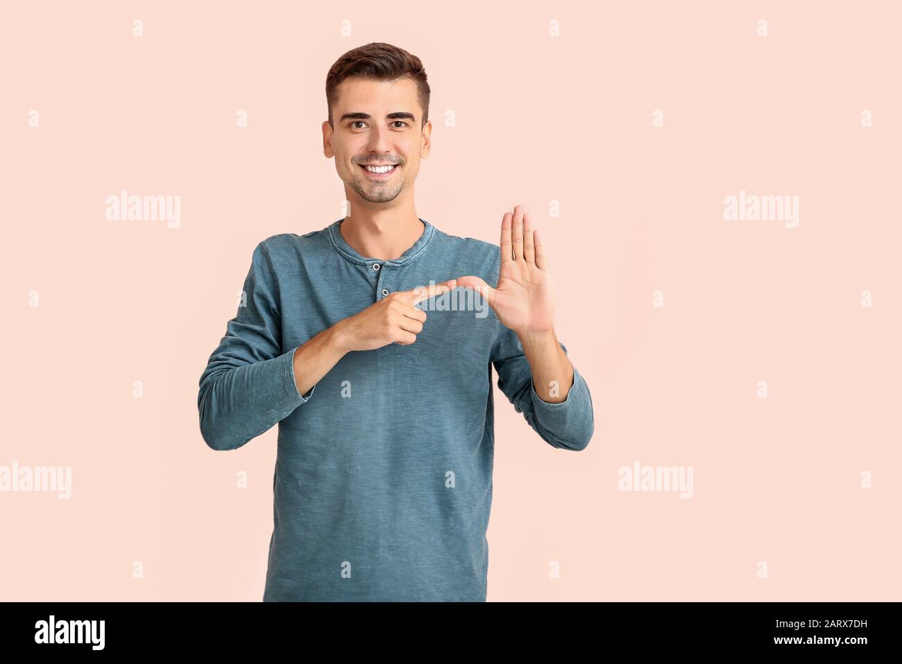 Young deaf mute man using sign language on color background Stock Photo