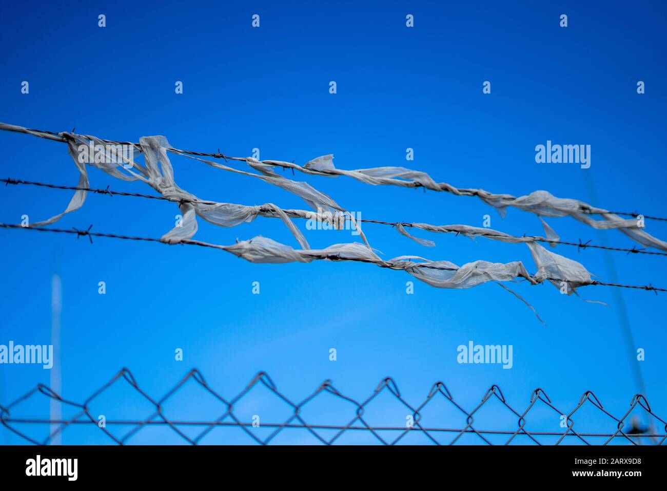 A barbed wire fence with tattered material tangled in it Stock Photo
