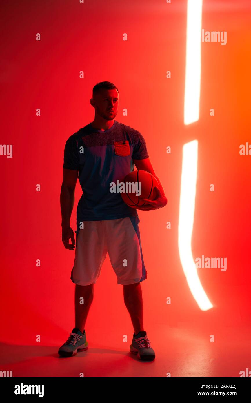 Young athletic man, basketball player stands holding ball in one hand
