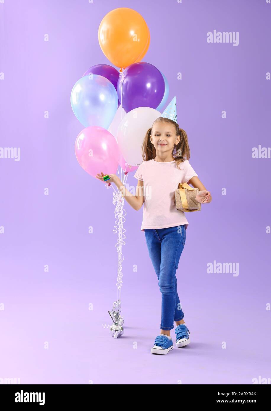Little girl with Birthday gift and party blower on color background ...