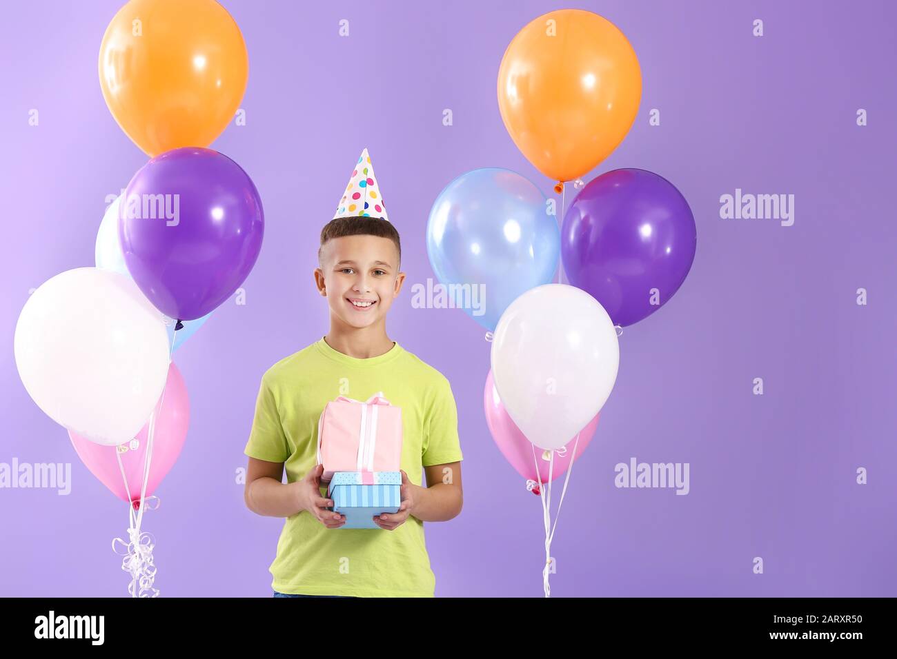 Little boy with Birthday air balloons and gifts on color background