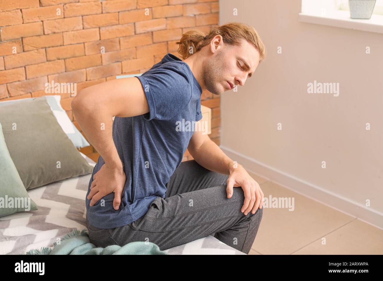 Young man suffering from back pain at home Stock Photo - Alamy