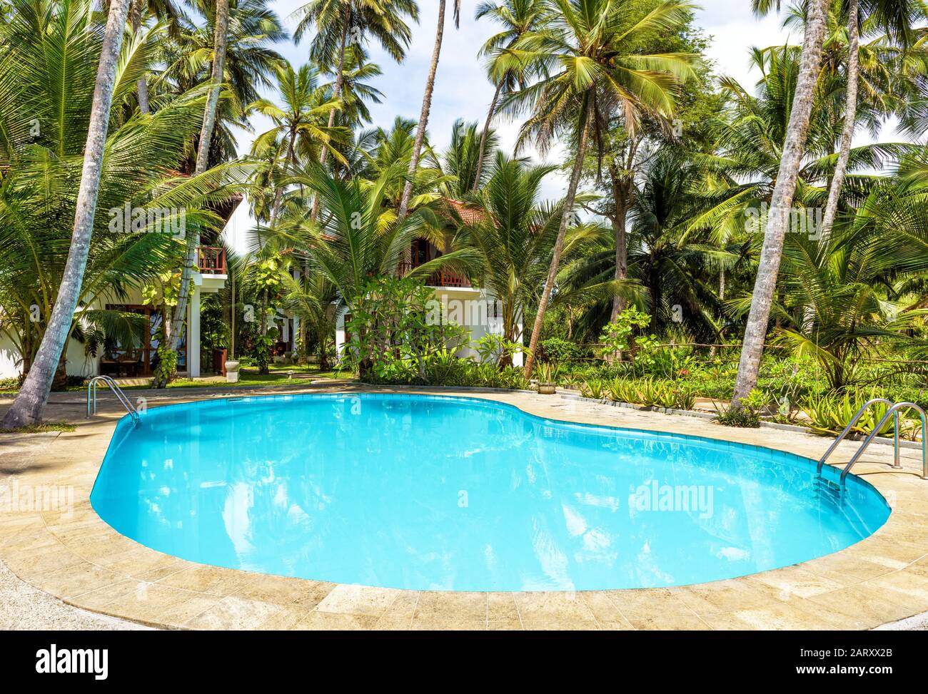 Tangalle, Sri Lanka - November 4, 2017: Swimming pool and houses in tropical hotel. Idyllic sunny place among palm trees. Picturesque hotel to relax i Stock Photo