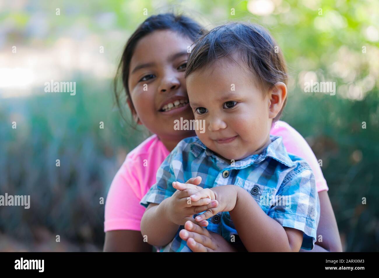 Older sister holding her little brother close to her and hugging him to show affection. Stock Photo
