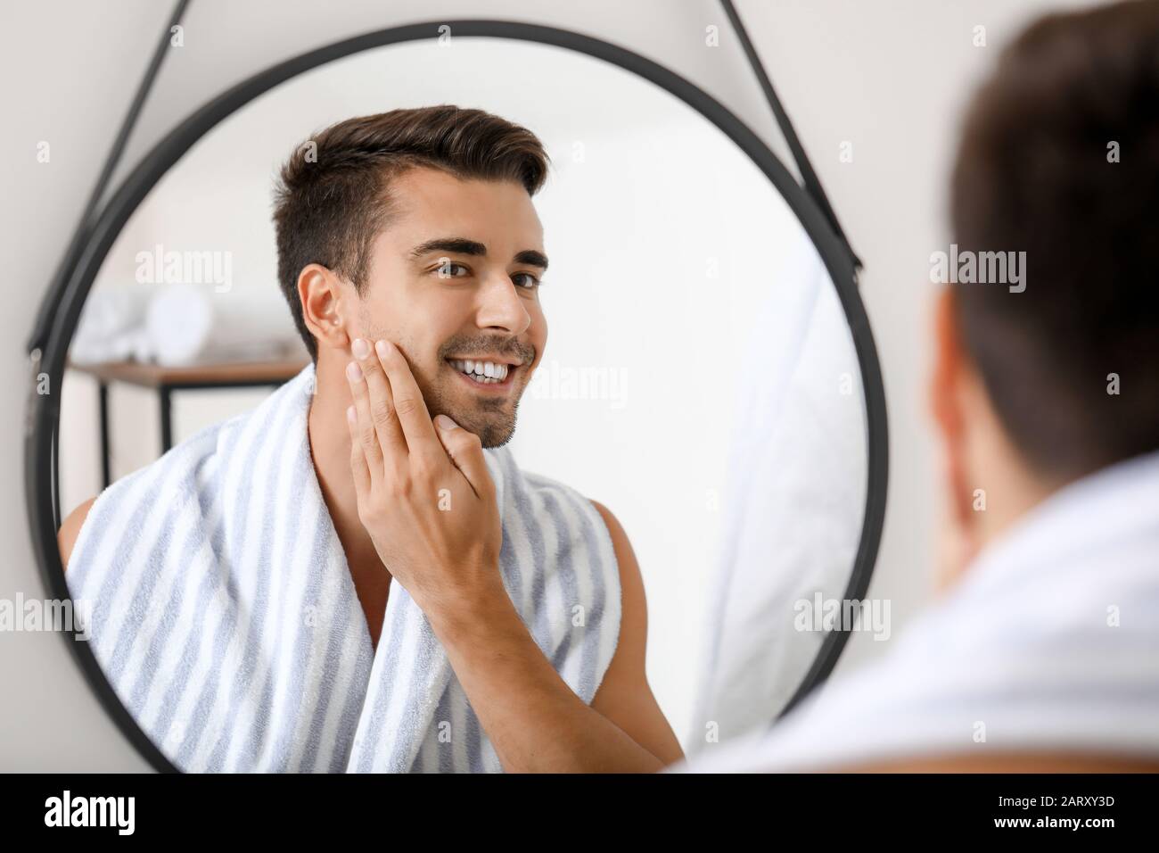 Handsome young man looking in mirror after shaving at home Stock Photo