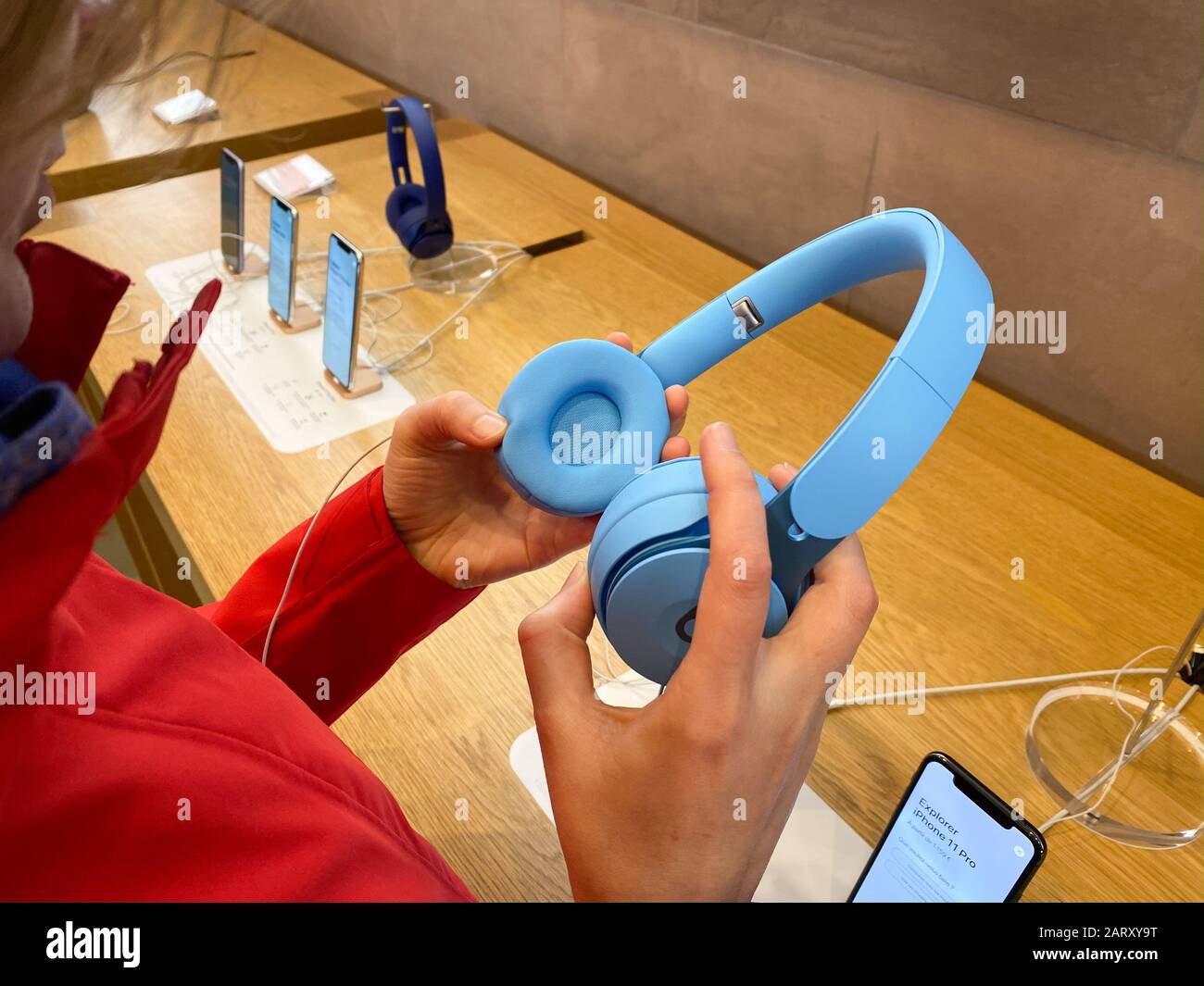 Paris, France - Nov 02, 2019: Woman in red coat inside Apple Computers Store testing admiring the new latest Beats by Dr Dre Solo Pro Active Noise Cancelling headphones Stock Photo