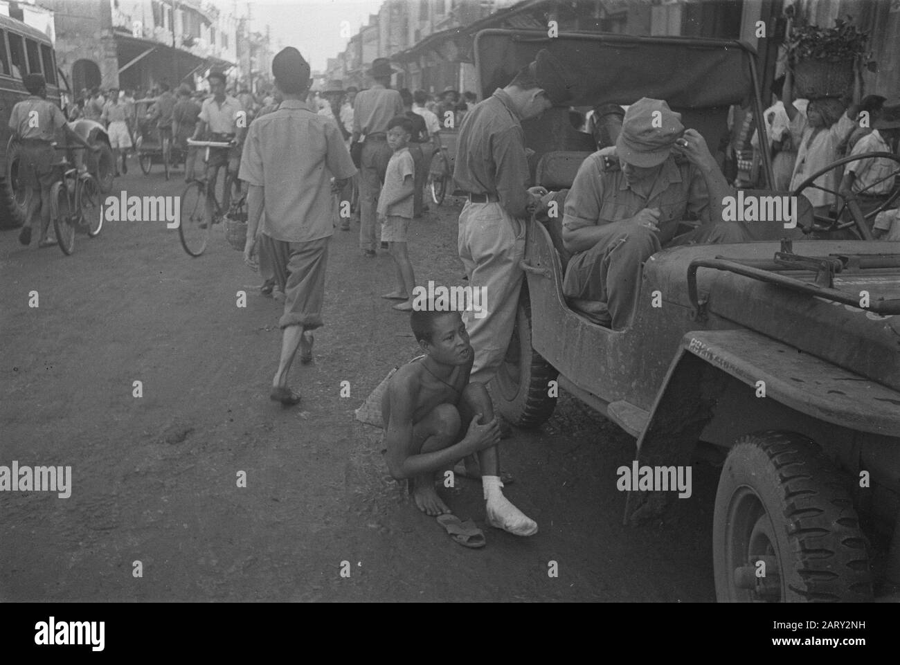Photo Reportage Palembangs  Two Dutch soldiers, one of which a 2nd lieutenant in a jeep in a shopping street in Palembangs. A young man with an injured foot comes begging? Date: 1947 Location: Indonesia, Dutch East Indies Stock Photo
