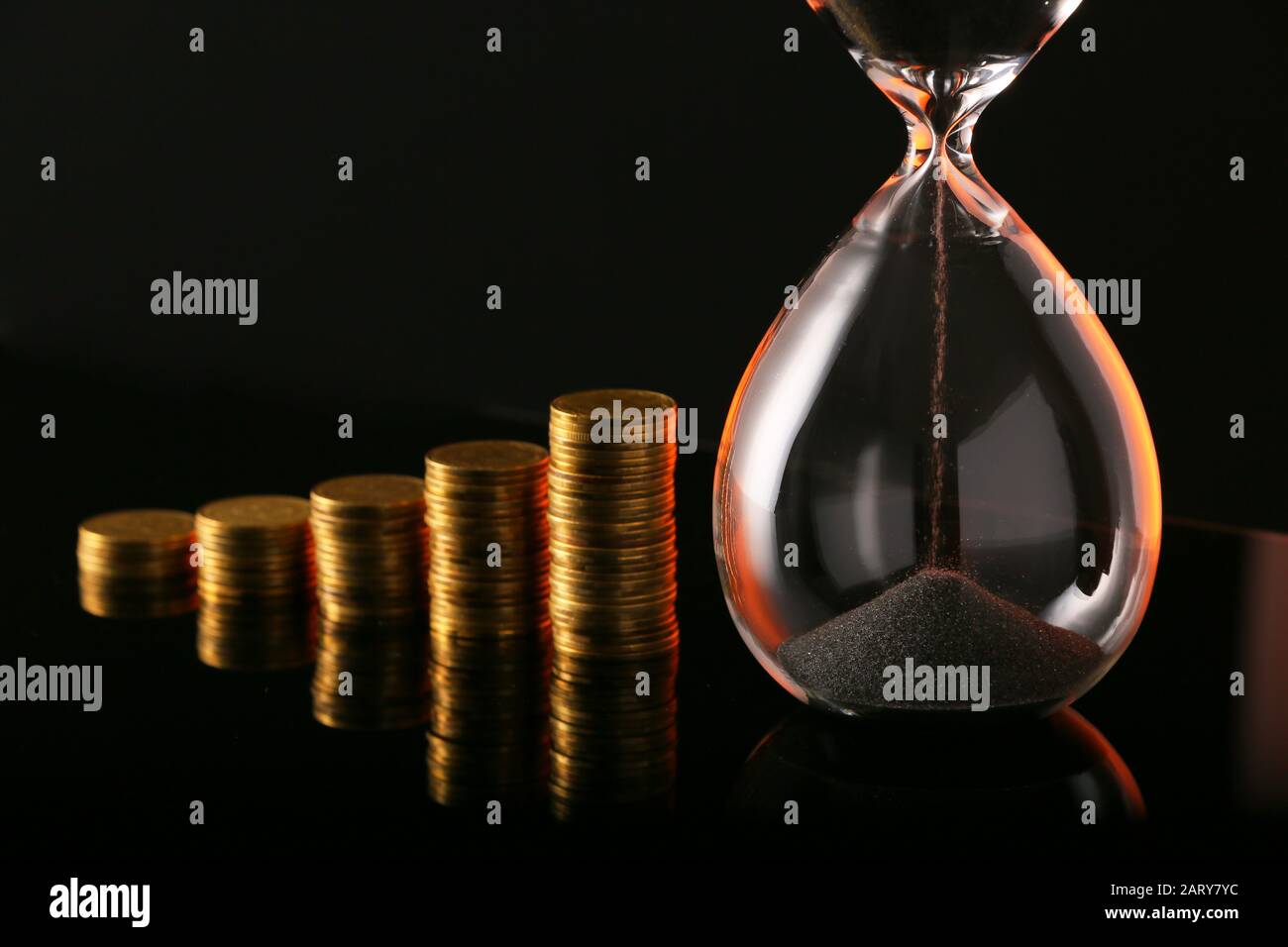 Hourglass with coins on dark background Stock Photo - Alamy