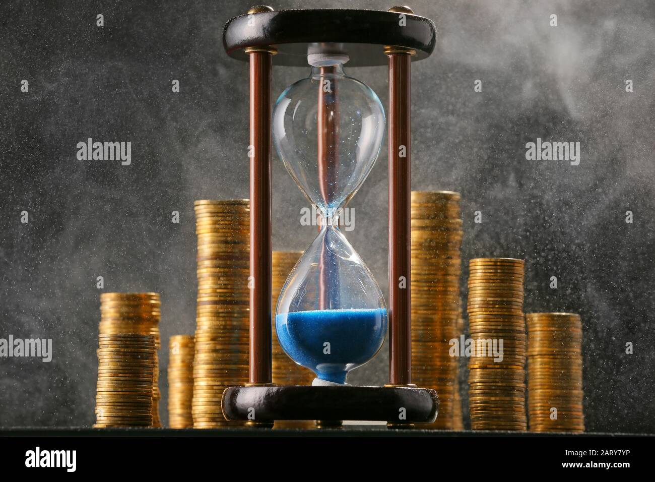 Hourglass with coins on dark background Stock Photo - Alamy