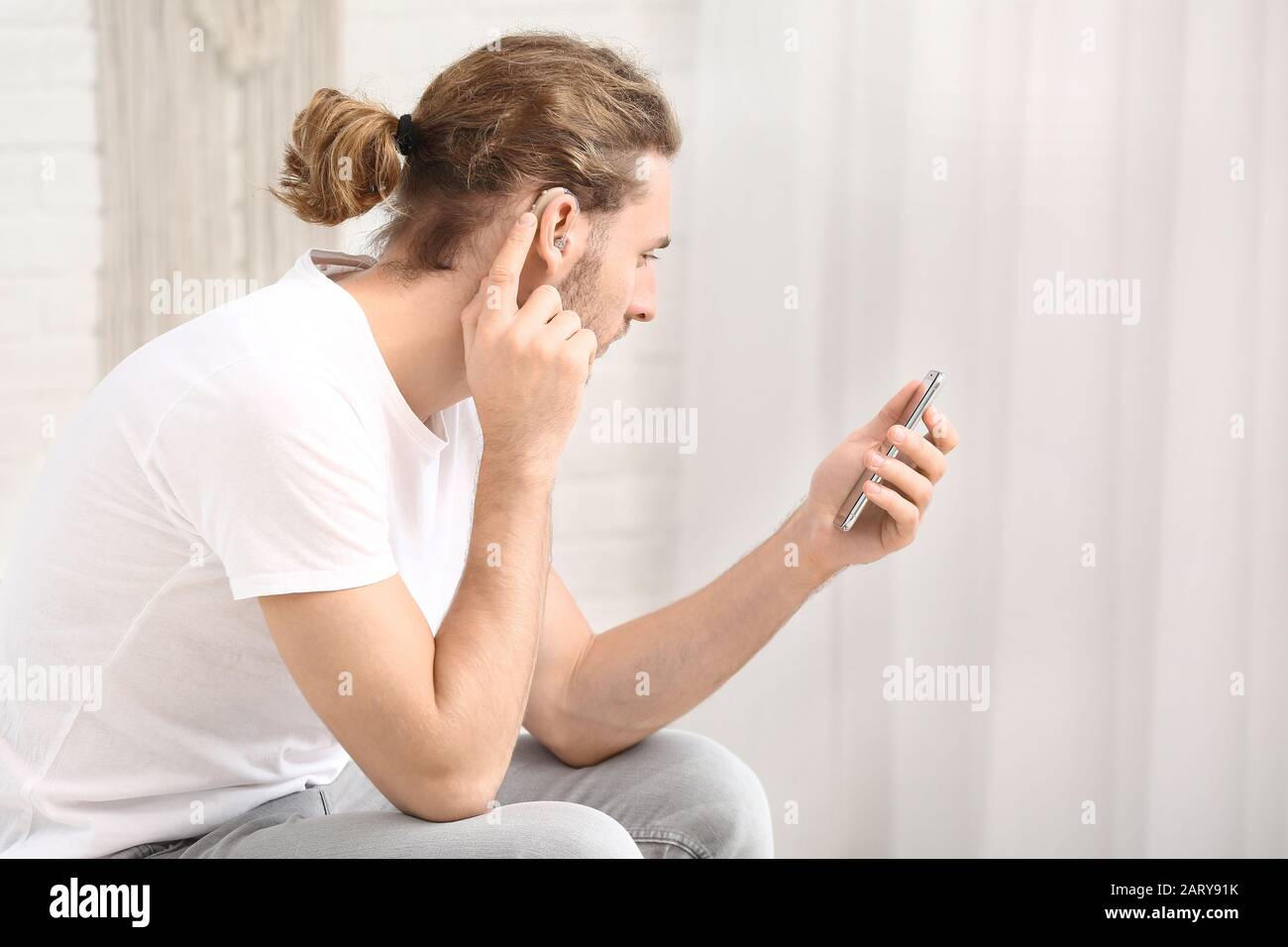 Young man with hearing aid using mobile phone at home Stock Photo