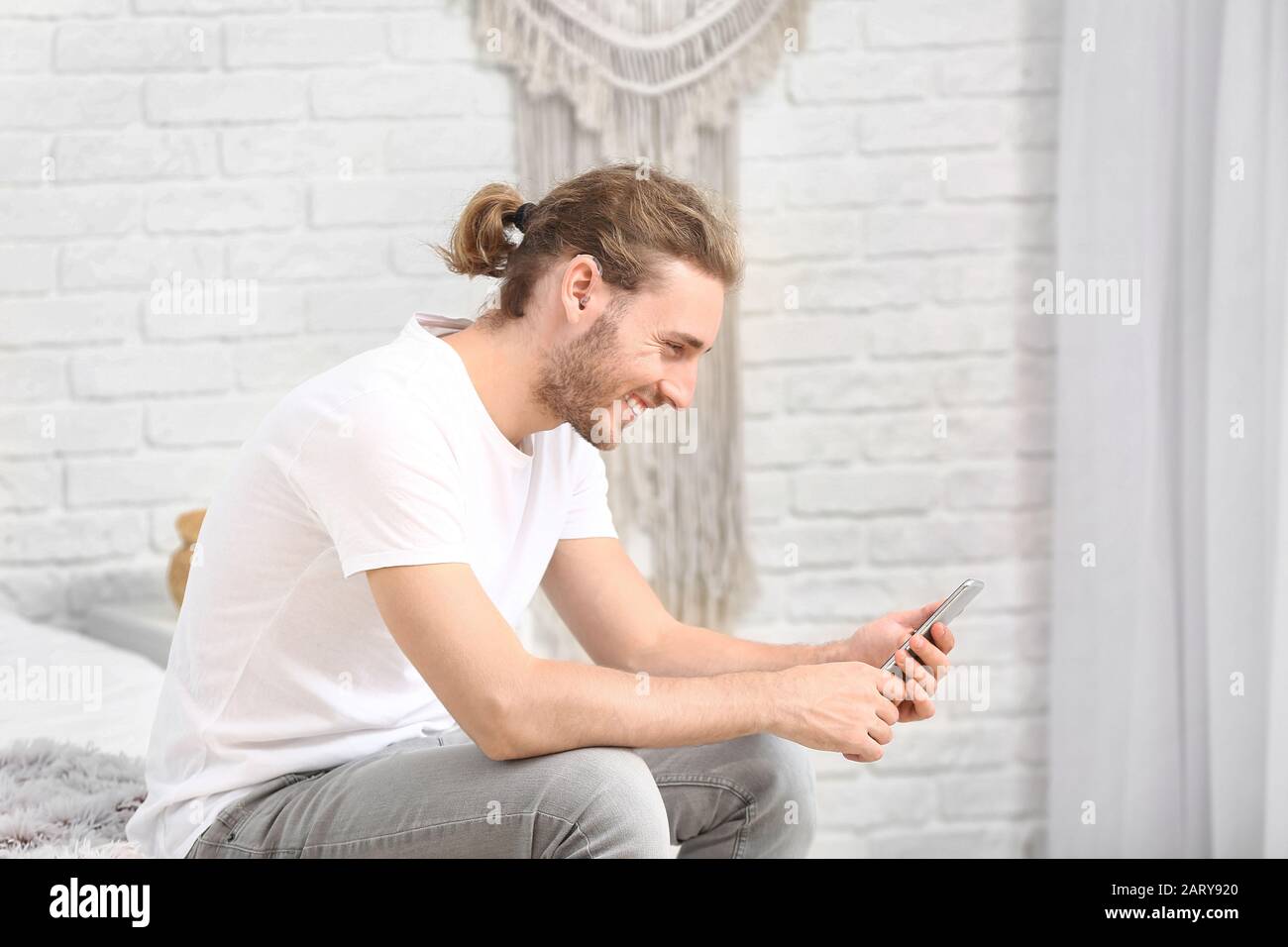 Young man with hearing aid using mobile phone at home Stock Photo