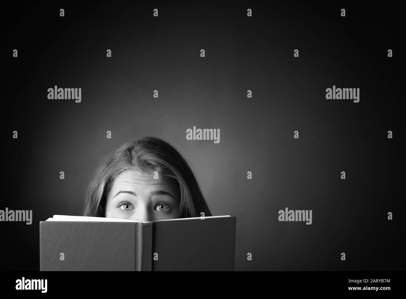 Black and white portrait of surprised teenage girl with book on dark background Stock Photo