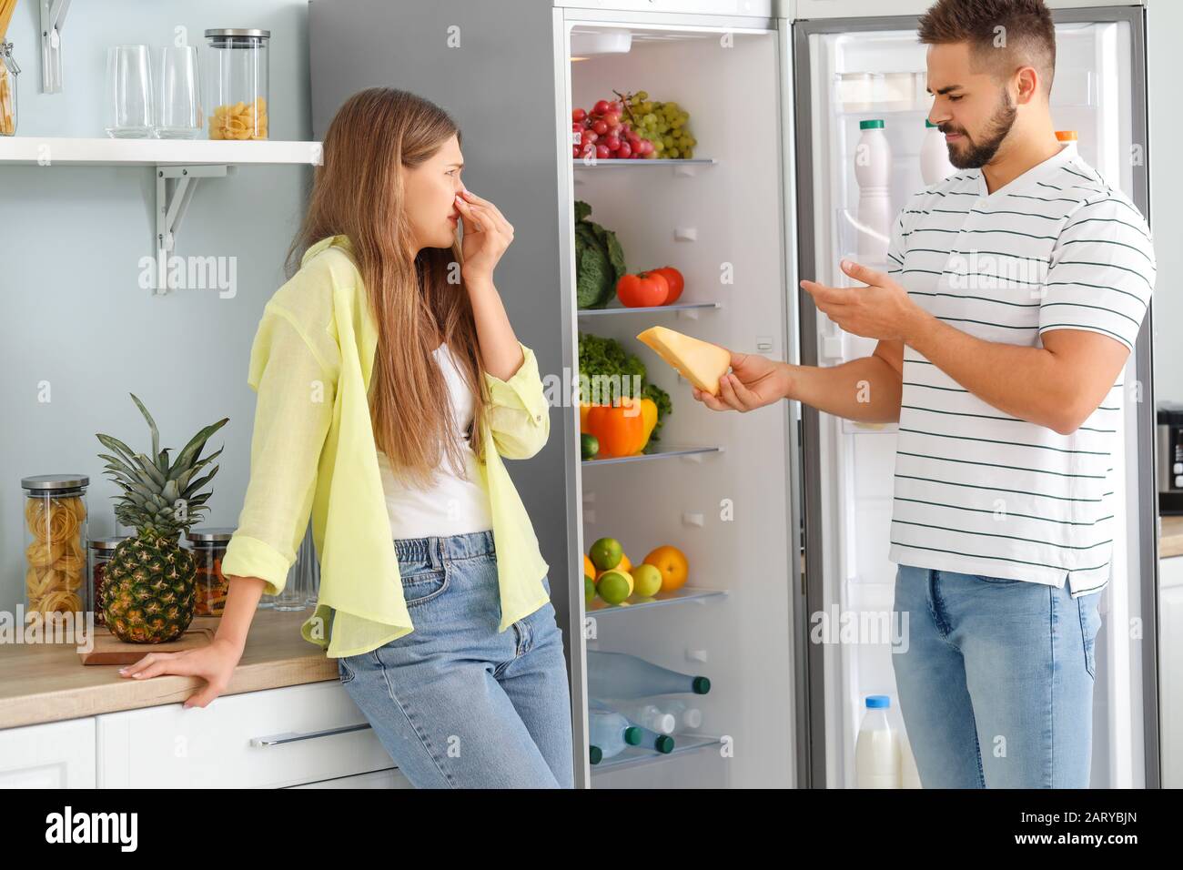 Young couple feeling bad smell from fridge in kitchen Stock Photo
