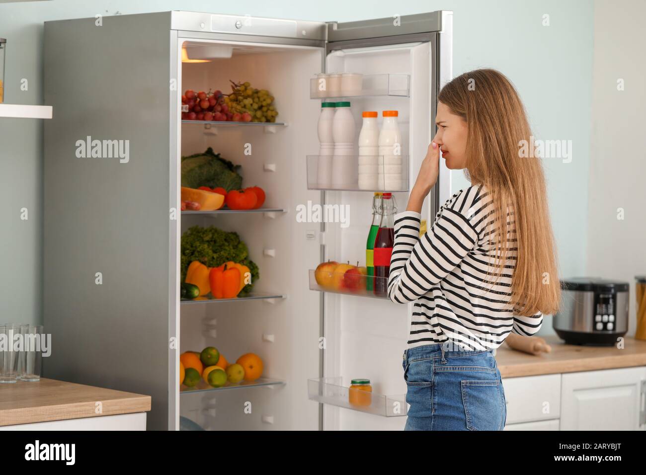 Woman feeling bad smell from fridge in kitchen Stock Photo