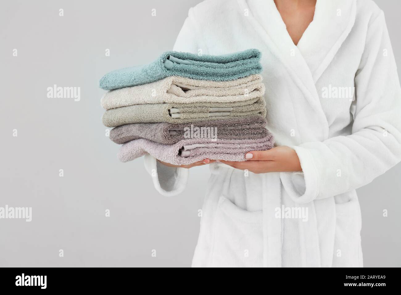 Woman holding stack of towels on light background Stock Photo