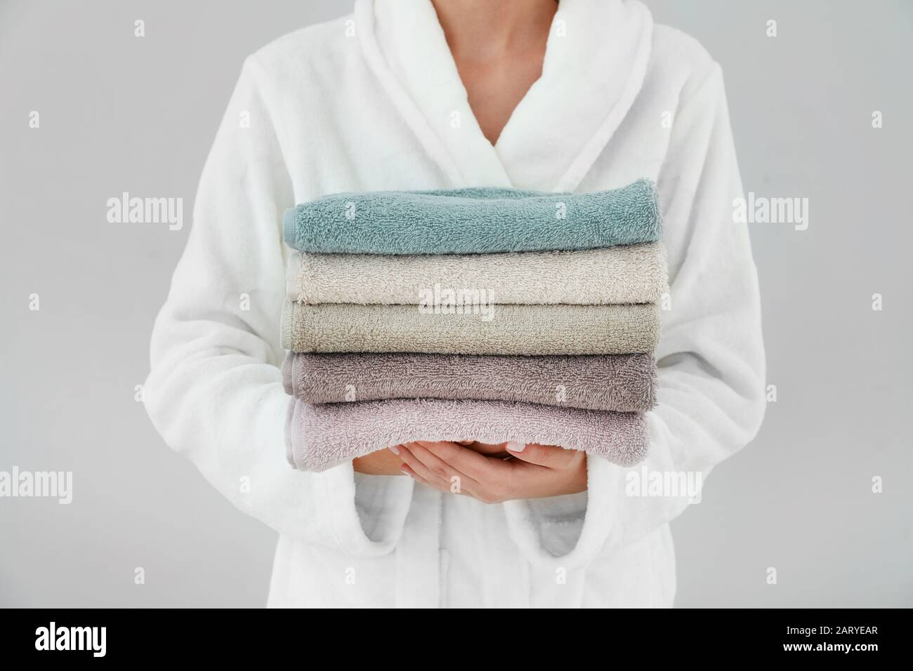 Woman holding stack of towels on light background Stock Photo