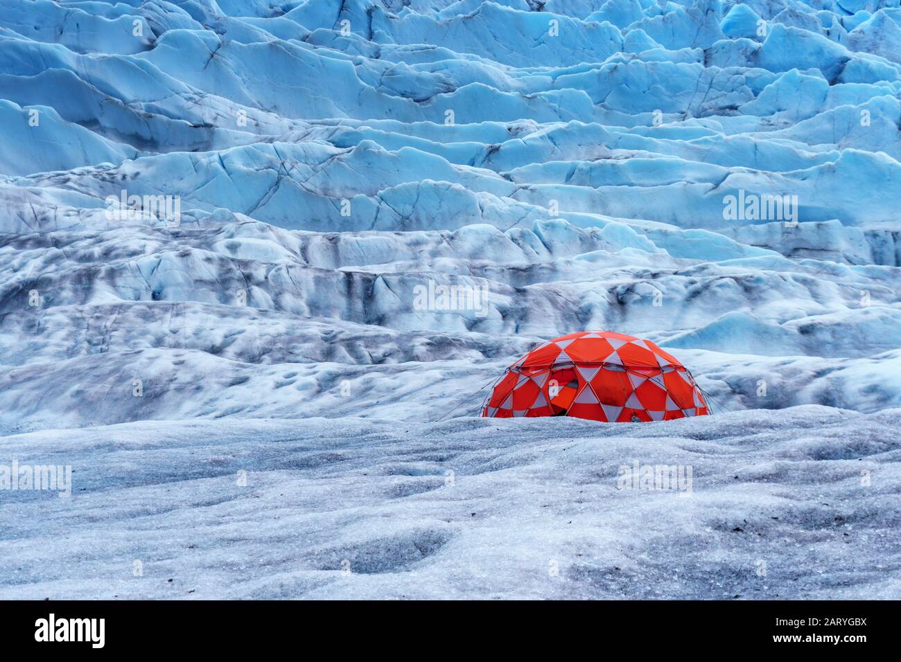 Red tent on the glacier. Excursion by helicopter in Juneau, Alaska. Extended glacier trek is hiking and ice climbing. Camp on the mountain. Stock Photo