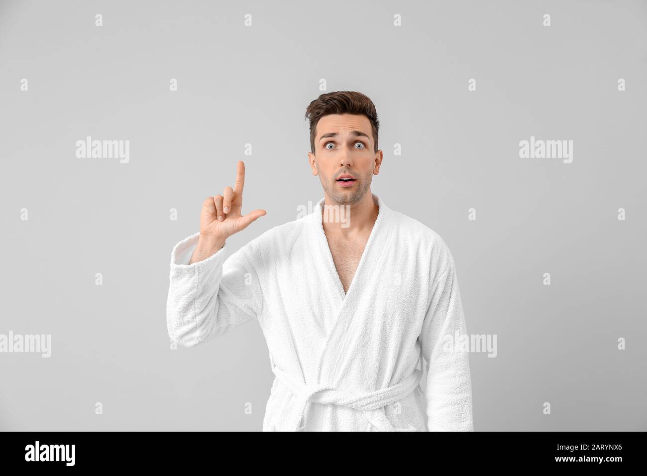 Surprised man in bathrobe pointing at something on grey background Stock Photo