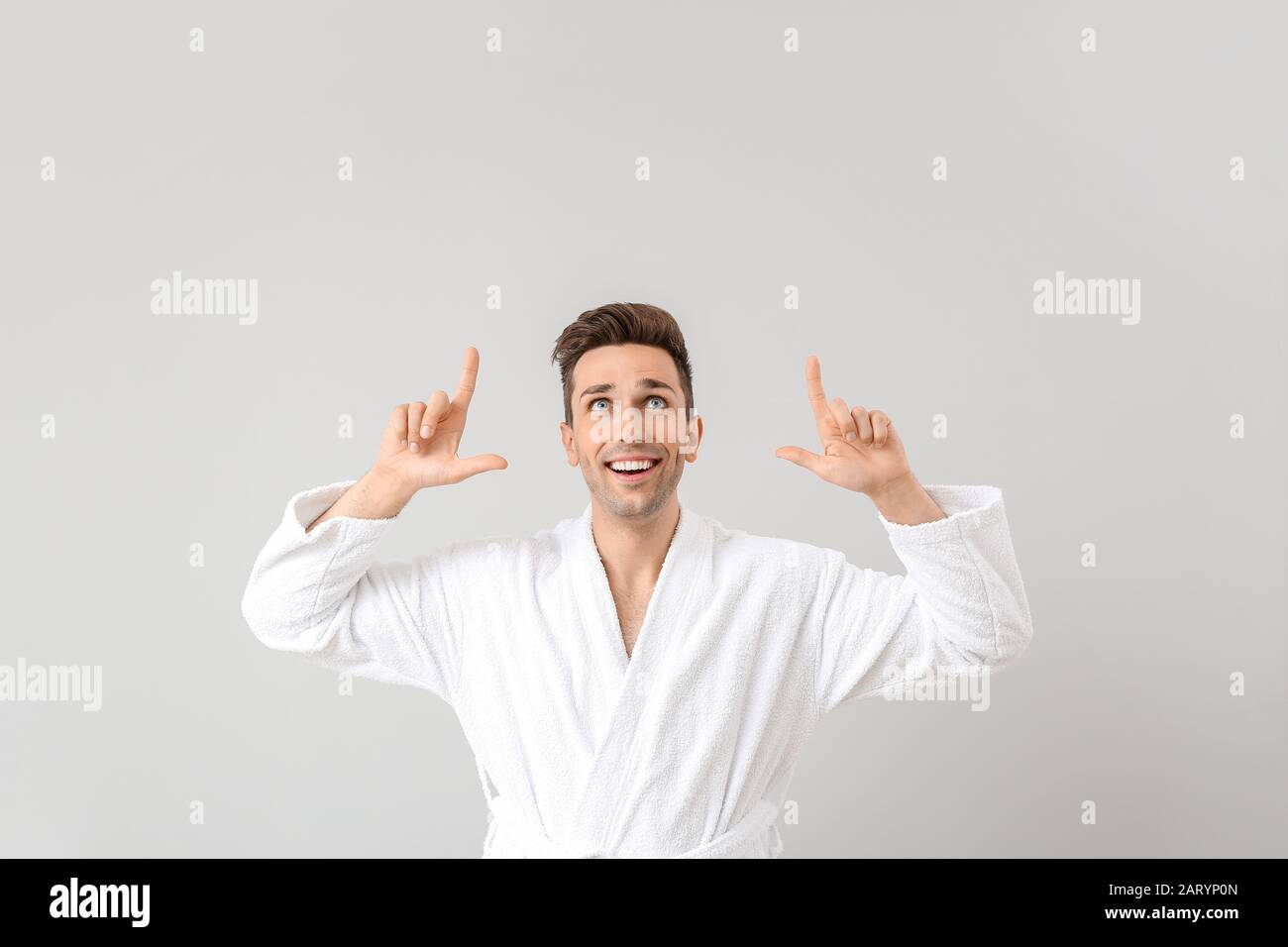 Handsome man in bathrobe pointing at something on grey background Stock Photo