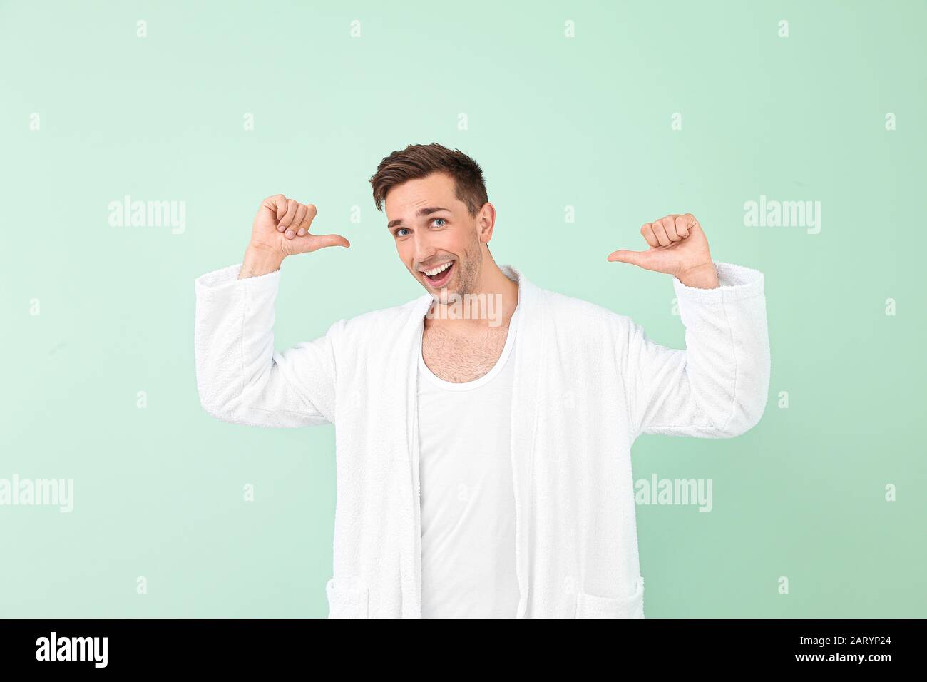 Happy man in bathrobe showing something on color background Stock Photo