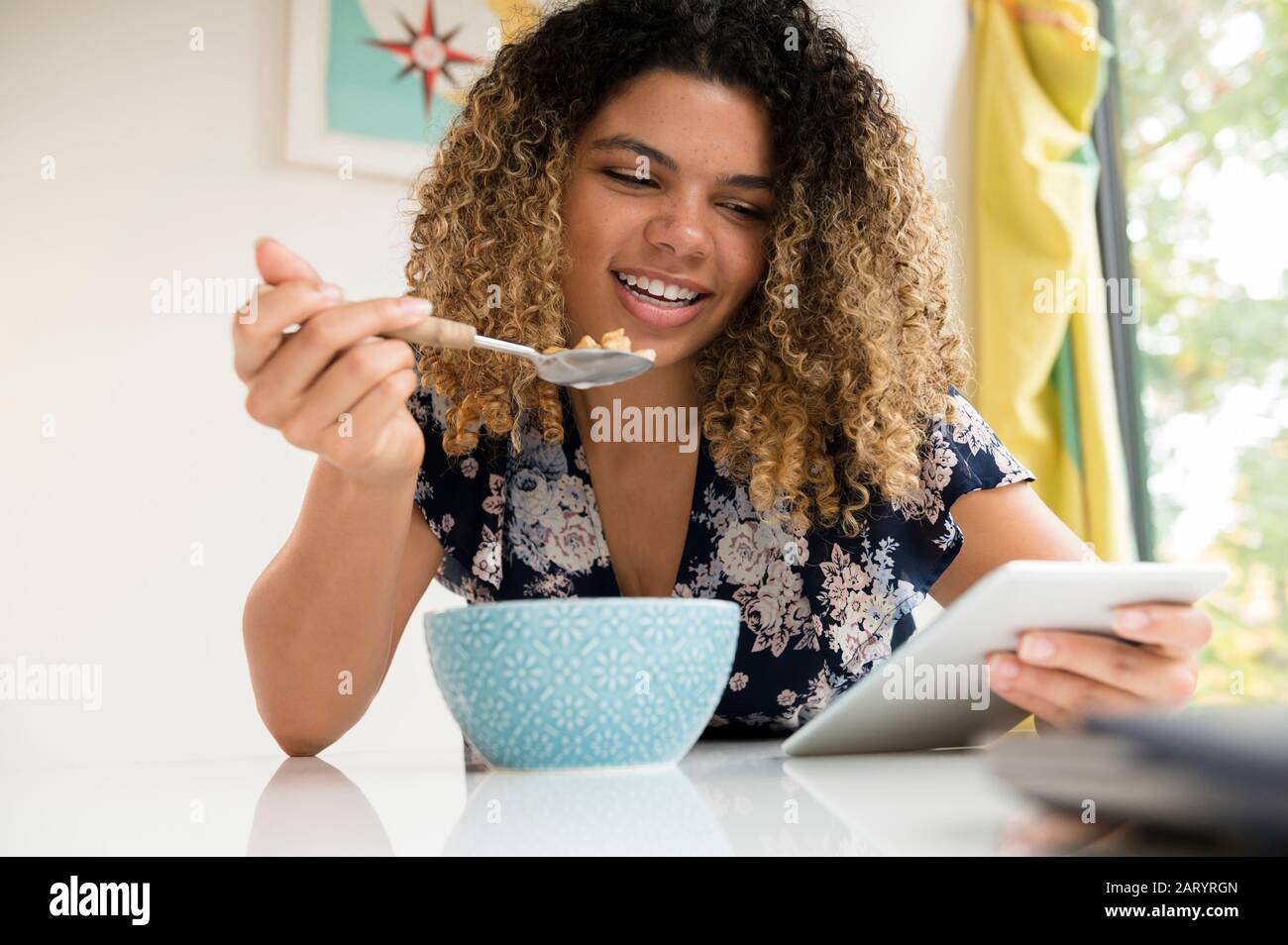 Smiling woman using tablet while eating breakfast Stock Photo